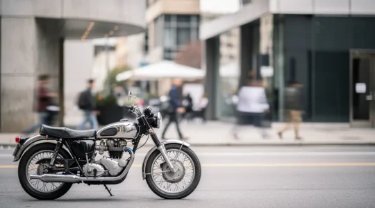 Vue latérale d'une moto vintage stationnée dans un environnement urbain avec des silhouettes humaines floues en arrière-plan