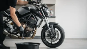 Motard en gants réalisant une vidange sur une moto dans un garage propre, avec des outils posés à côté et un grand espace vide pour un titre.